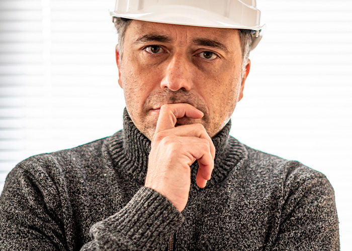 Thoughtful male manager in a gray sweater and white hard hat, reflecting on ridiculous employee complaints received by HR.