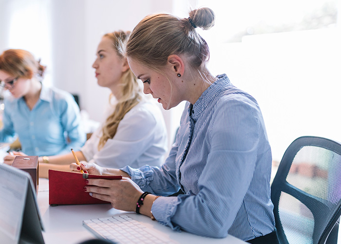 Young professional writing in a notebook at office desk, illustrating ridiculous complaints managers and HR received from employees.