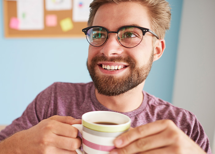 Young man with glasses smiling and holding a coffee cup, representing ridiculous employee complaints to managers and HR.
