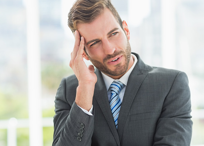 Businessman in a gray suit with a striped tie, looking frustrated while thinking about ridiculous employee complaints.