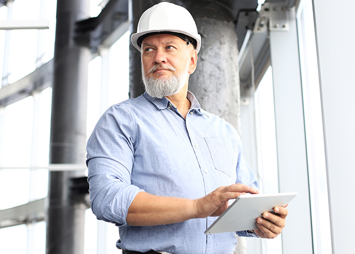 Construction manager wearing a hard hat using a tablet, representing employee complaints received by managers and HR.