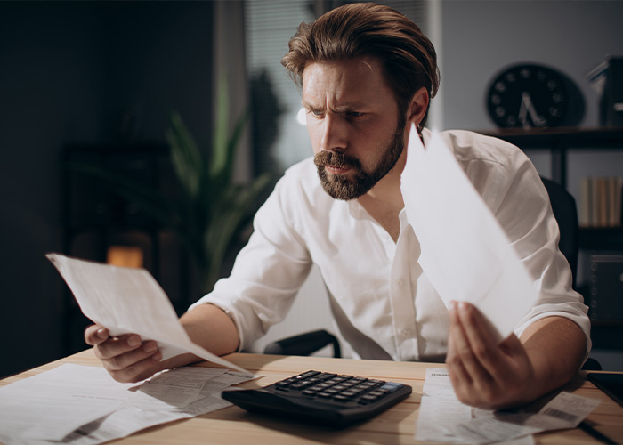 Man in a white shirt looking frustrated while reviewing documents and bills, illustrating facts people are tired of explaining.