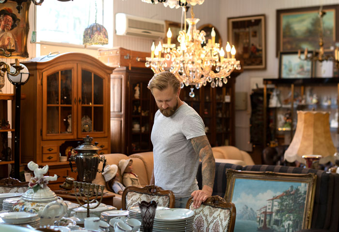 Man with tattoos in a vintage room exploring antiques, revealing unexpected things people learned about the rich lifestyle.