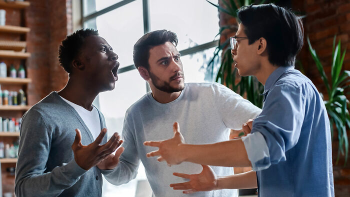 Three men having an intense discussion indoors, sharing experiences that seem bizarre to women but normal to men.
