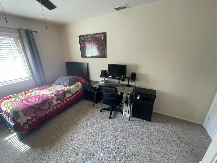 Simple bedroom setup with a floral blanket bed and basic desk workstation, reflecting men's normal but bizarre habits to women.
