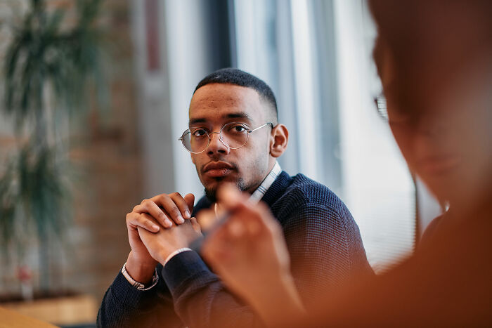 Man wearing glasses and a sweater listening intently in a meeting, illustrating things men find normal but women find bizarre.