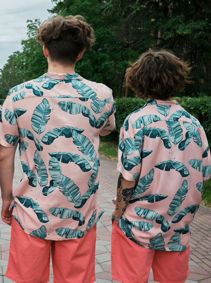 Two men wearing matching tropical leaf print shirts and coral shorts walking outside, highlighting things normal to men but bizarre to women.