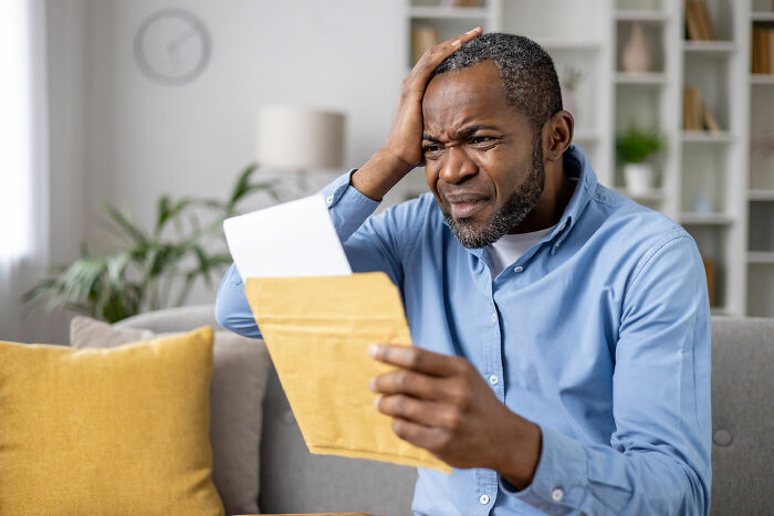 Man in blue shirt sitting on couch, looking confused and worried while reading a letter about creepy real things witnessed.