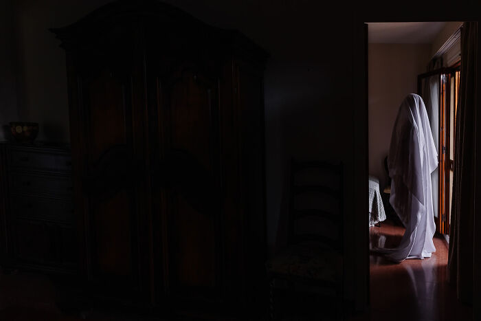 Ghostly figure covered in white sheet standing near window in a dark room, evoking creepy real-life encounters.