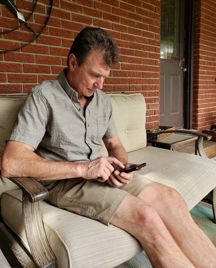Man sitting on porch sofa using phone, illustrating people sharing the creepiest real things they witnessed or heard about.