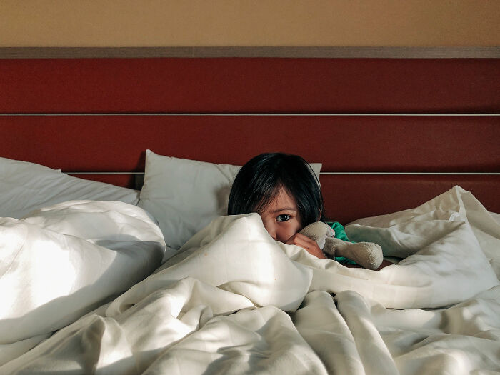 Child hiding under bed covers holding a stuffed toy, evoking the creepiest real things witnessed or heard about.