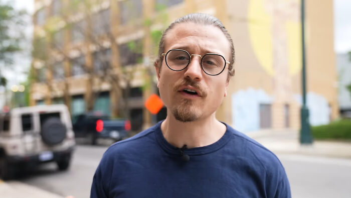 Man with glasses and a beard speaking outdoors, representing people share unsubscribed YouTubers in an urban setting.