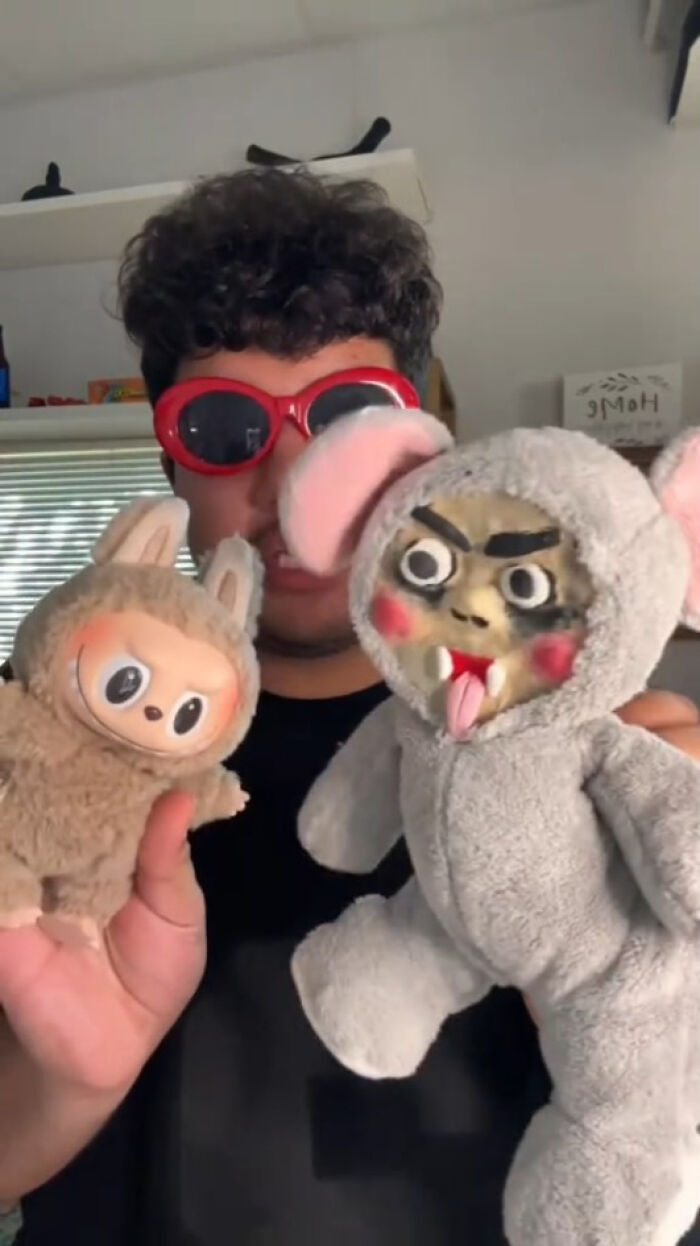 Person wearing red sunglasses holding two Labubus fakes, creepy and nightmarish stuffed toys in a home setting.