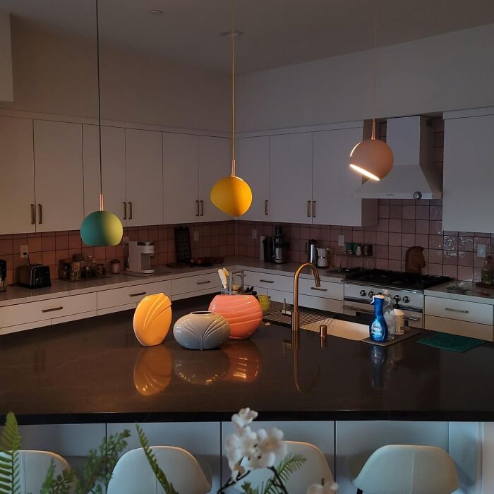 Modern kitchen with colorful pendant lights and unique decor pieces on the island in a living space revamp project shared online.