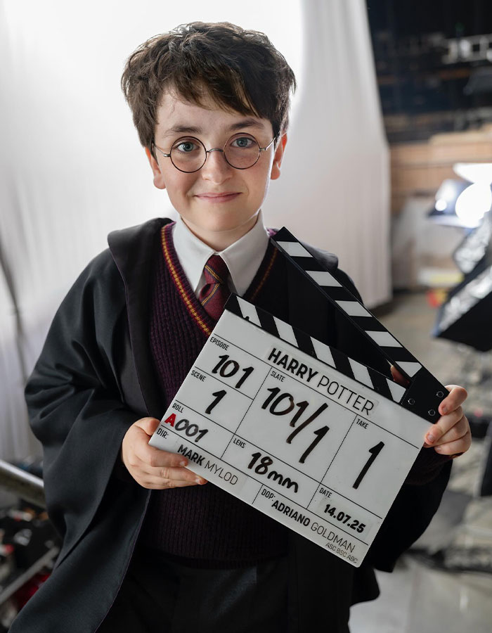 Young actor dressed as Harry Potter holding a clapperboard on the set of HBO's upcoming Harry Potter show.