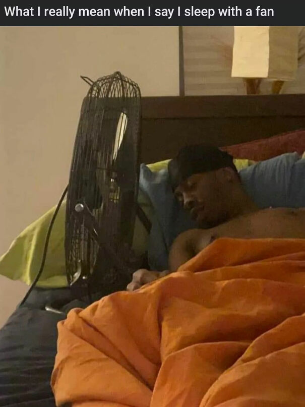 Man sleeping in bed next to a fan, capturing a funny summer meme about staying cool indoors during hot weather.