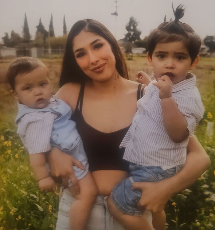 Young mother holding two toddlers outdoors, related to after baby lost his life in car incident and court charges. - 1