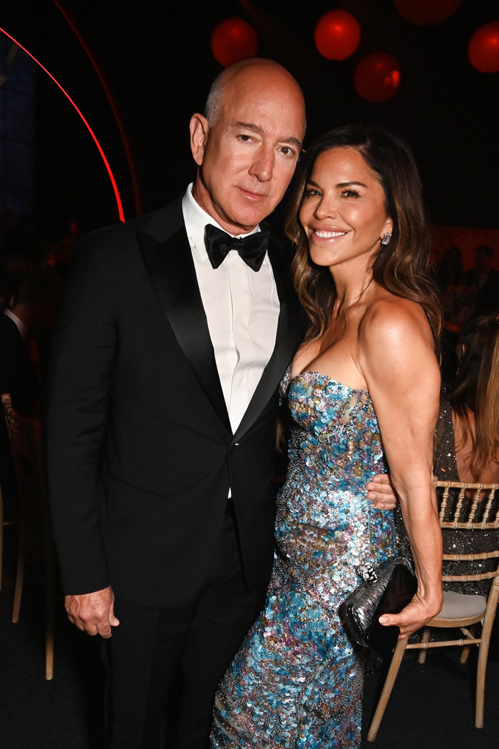 Jeff Bezos wearing a tuxedo with hair, posing with Lauren S&aacute;nchez in a colorful dress at an evening event.