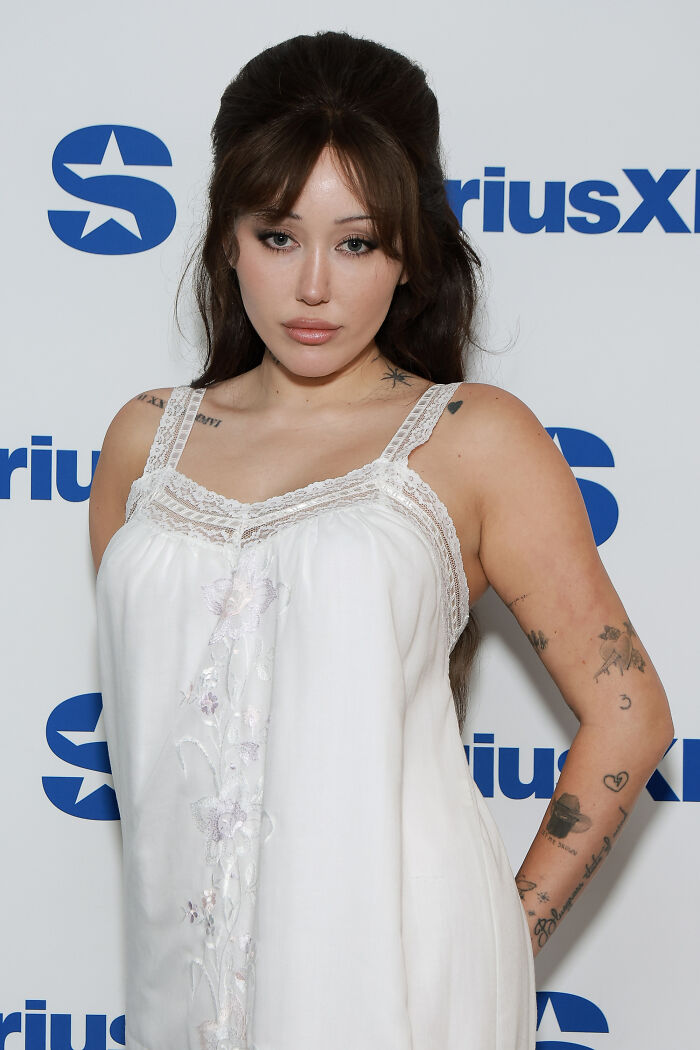 Noah Cyrus posing in a white dress at SiriusXM event, sparking plastic surgery rumors with striking transformation. Noah Cyrus posing in a white dress at SiriusXM event, sparking plastic surgery rumors with striking transformation.