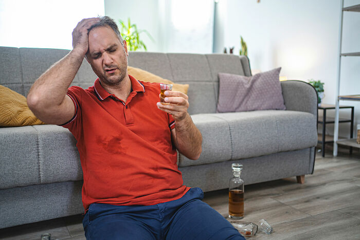Man sitting on floor with drink, looking distressed and stressed, illustrating people who ran away from home experiences. - 2