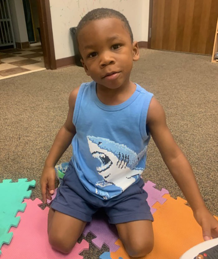 3-year-old boy in temporary foster care sitting on floor, wearing blue tank top with shark design and navy shorts. 3-year-old boy in temporary foster care sitting on floor, wearing blue tank top with shark design and navy shorts.