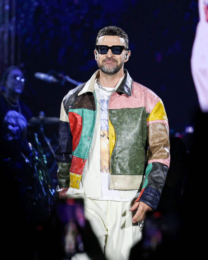 Justin Timberlake performing on stage during Romania show, wearing colorful jacket and sunglasses.