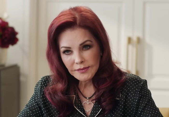 Priscilla Presley, 80, with red hair and dark polka dot blouse, looking downcast during a rare public outing. Priscilla Presley, 80, with red hair and dark polka dot blouse, looking downcast during a rare public outing.