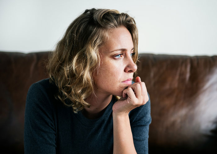 Woman with blonde curly hair sitting on a sofa, looking thoughtful and concerned, related to bride cancelling guest resort room. - 8