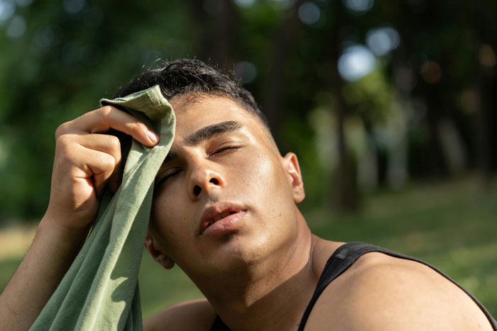 Young man wiping sweat from forehead outdoors, demonstrating tips to stay safe and alive in a hot environment.