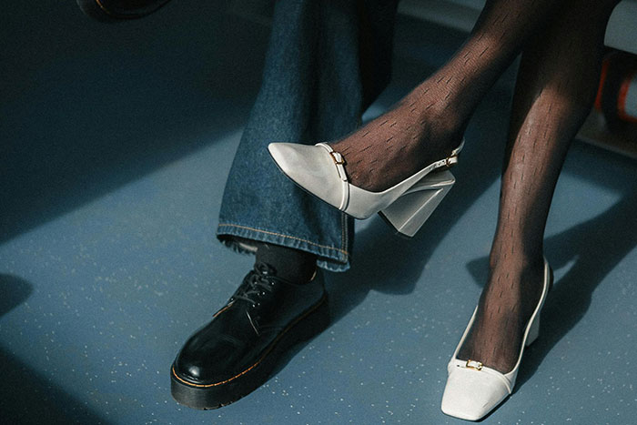 Close-up of big burly men and women’s feet, highlighting contrast in footwear and microfeminisms in a casual setting.