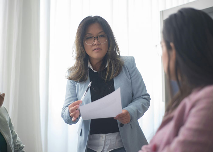 Woman in glasses discussing work with colleagues, illustrating micromanagement in a tense workplace setting.
