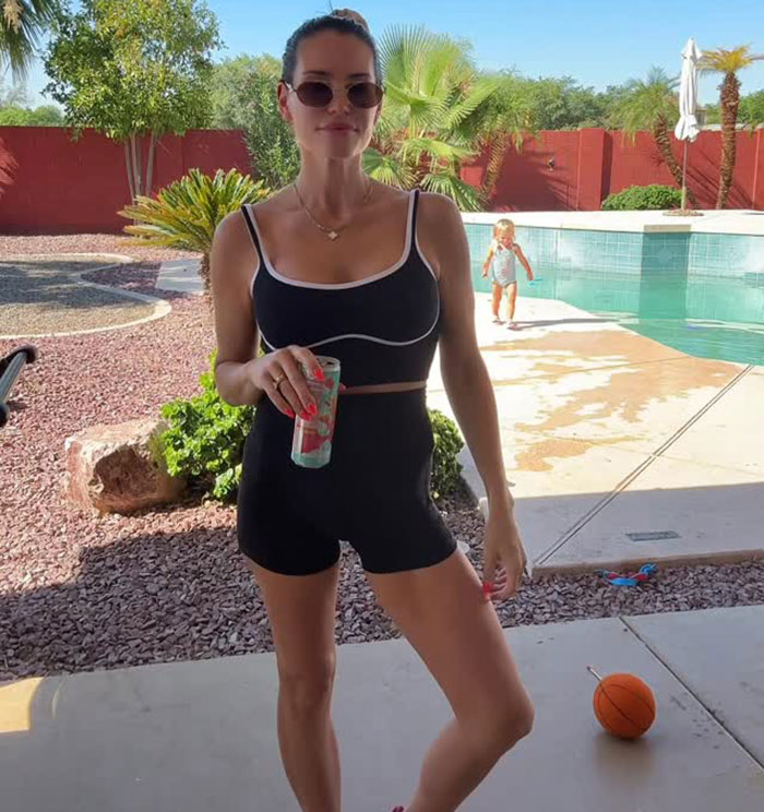 Woman with 3 kids in black activewear by pool enjoying a drink after stunning mommy makeover transformation.