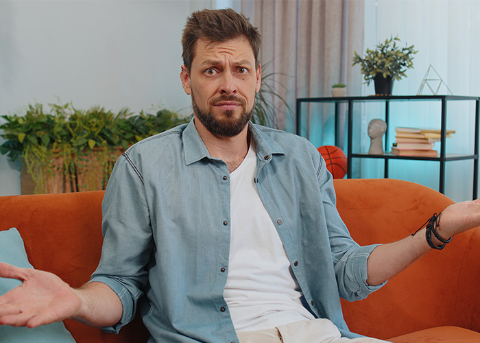 Man sitting on orange couch with confused expression, illustrating former employees revealing crazy secrets concept. - 3