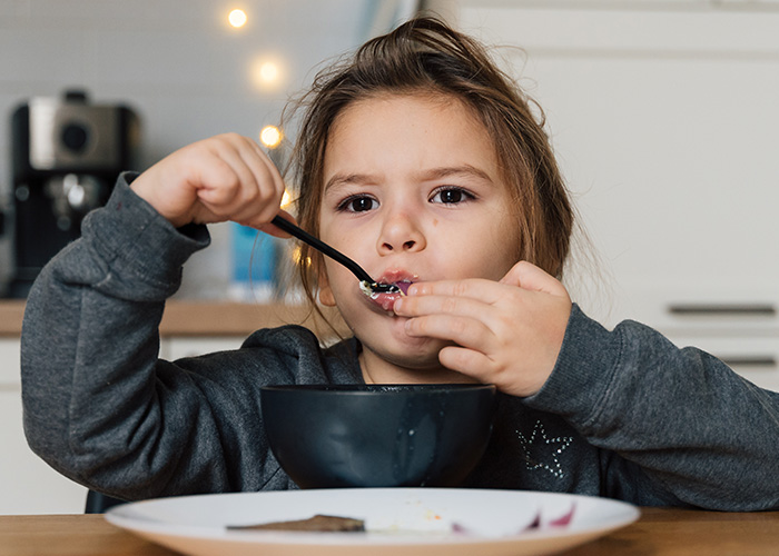 Young child eating from a bowl while parents reveal hilarious lies they tell their kids in a cozy kitchen setting.