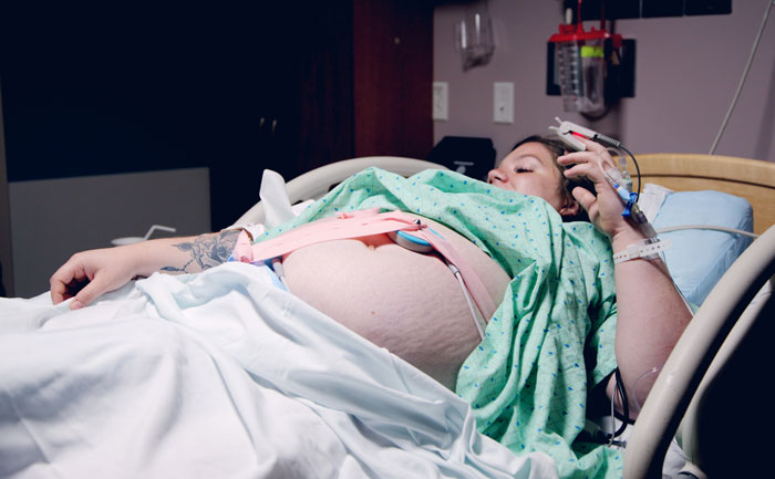 Woman upset in hospital bed, undergoing labor with medical monitoring equipment attached, showing distress during birth.