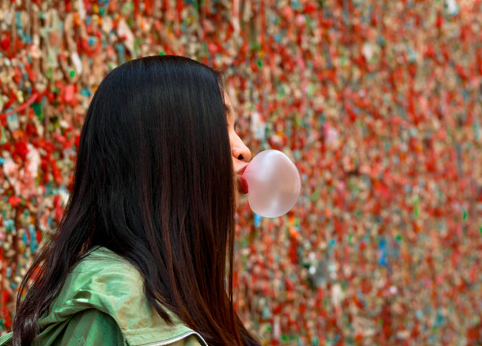 Woman blowing bubble gum in front of a colorful gum wall, illustrating bizarre laws including a Norwegian town that banned death. - 2
