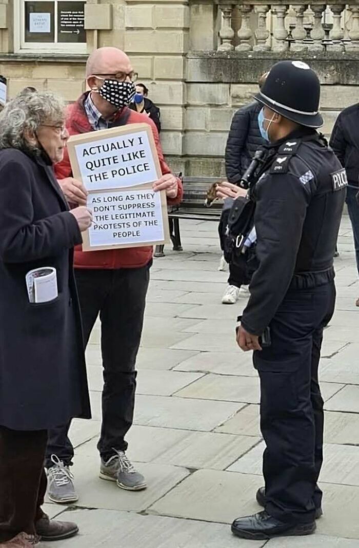 Man holding a protest sign talking to a police officer wearing a face mask in a public square showing positivity.