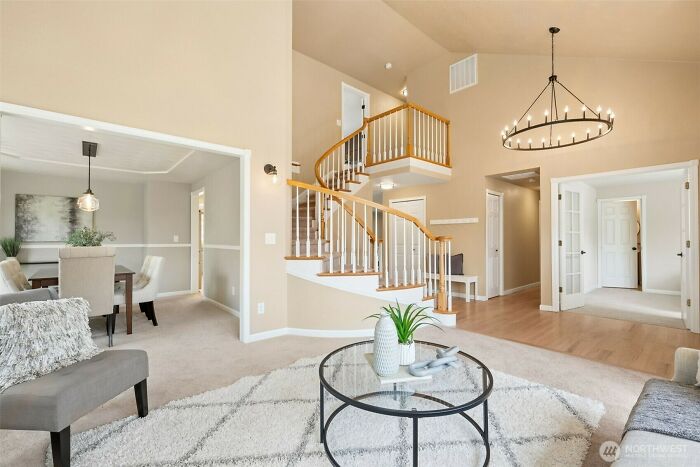 Bright living room with a glass coffee table and wooden spiral staircase in a stylish home interior design.