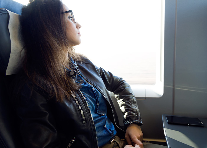 Young woman wearing glasses and leather jacket looking thoughtfully out a train window, tired of explaining facts to others.