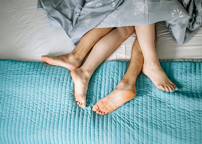 Couple's intertwined feet under blanket on bed, illustrating themes related to cheating stories and relationships.