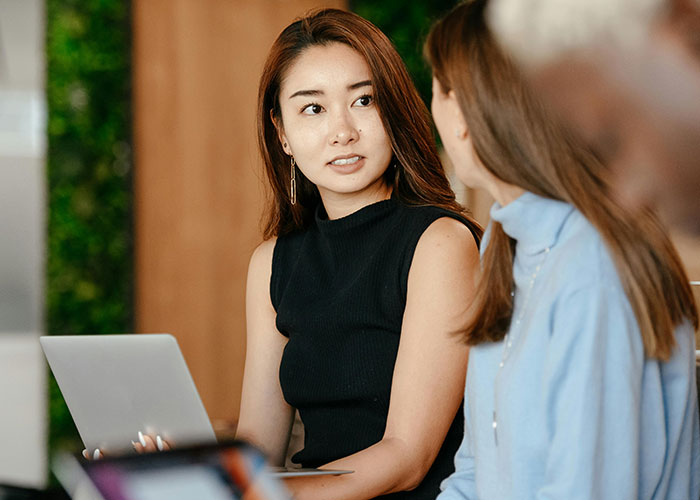 Two women discussing work on a laptop, illustrating micromanagement challenges in a modern office environment.