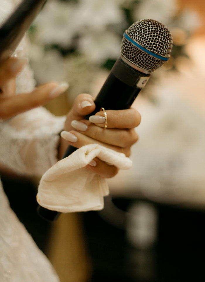 Close-up of a hand holding a microphone and a cloth at a wedding, capturing a moment during a speech or toast. - 35