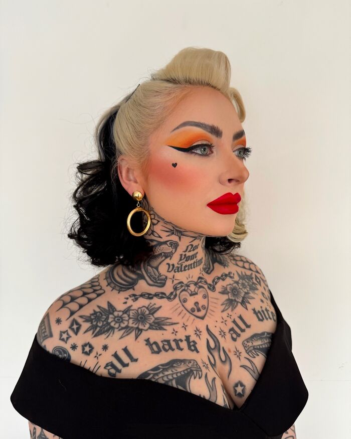 Woman with extensive tattoos covering chest and neck, showcasing body suit transformation and bold makeup with red lipstick.