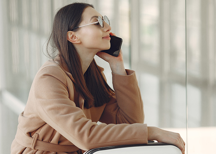 Young woman in sunglasses sitting with luggage, talking on phone, representing former employees revealing secrets. - 14