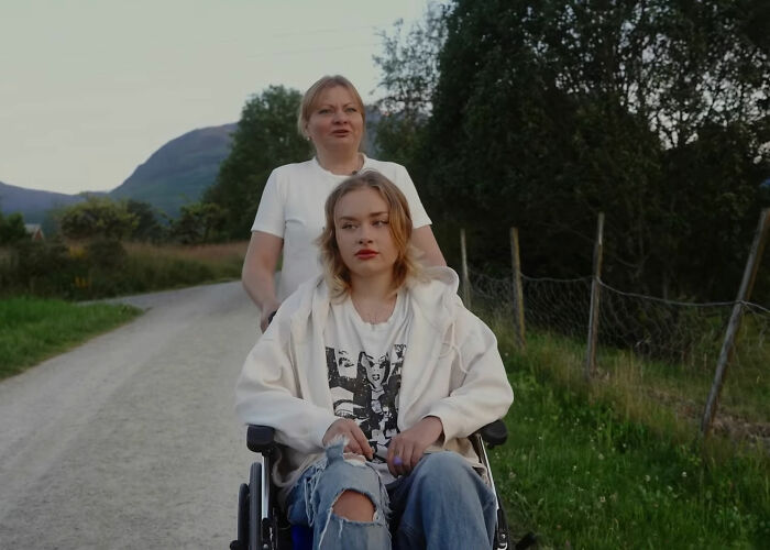 Mother pushing her daughter in a wheelchair along a rural path, illustrating model's mom revealing scalp injury and roadside dumping. - 10