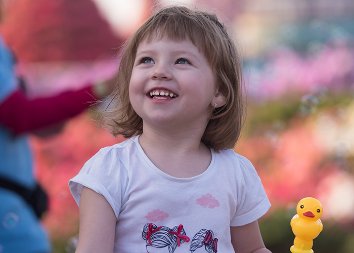 Smiling young girl outdoors holding a yellow toy duck, capturing moments of parents and kids sharing humorous lies.