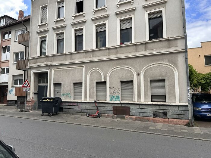 Old residential building with faded arch designs and graffiti, showing a failed creative home exterior renovation attempt.
