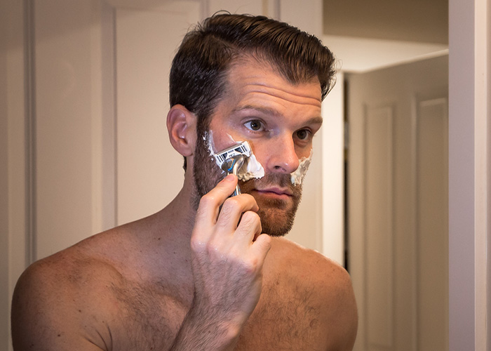 Man shaving his face in front of a bathroom mirror, illustrating facts people are getting tired of explaining to others.