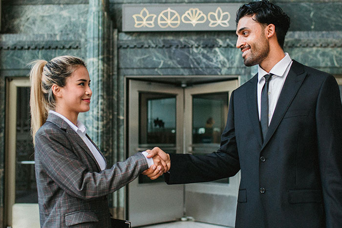 A woman and a big burly man shaking hands outside a building, illustrating microfeminisms in a professional setting.