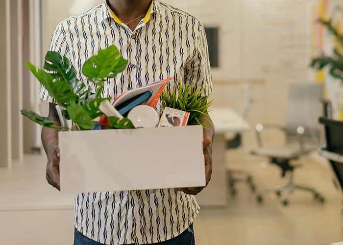 Man holding a box of personal belongings leaving an office, illustrating signs of micromanagement in the workplace.
